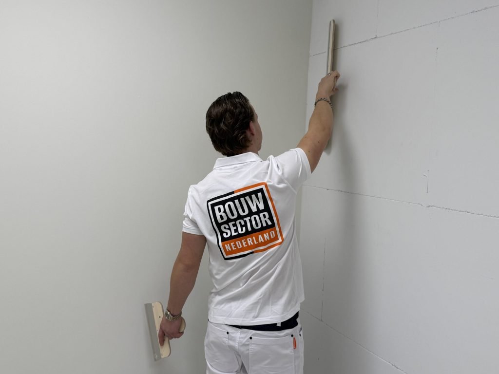 Stukadoor van Bouwsector Nederland zet een rij tegen de wand in een hoek van de kamer, met een plamuurmes in zijn andere hand