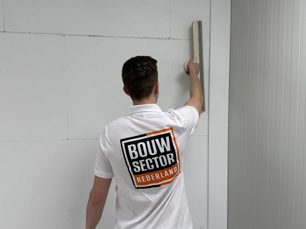 Stukadoor van Bouwsector Nederland in wit werkshirt trekt een verse laag op de muur glad met een brede spaan