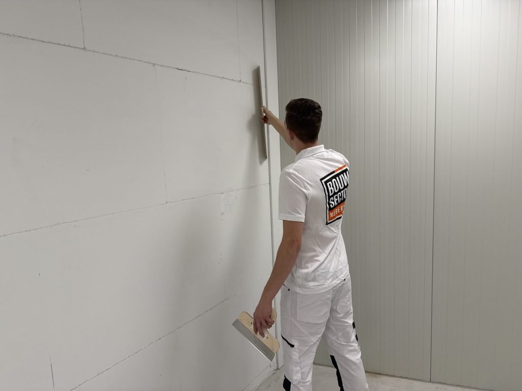 Stukadoor van Bouwsector Nederland controleert met een lange spaan of een hoge wand vlak is
