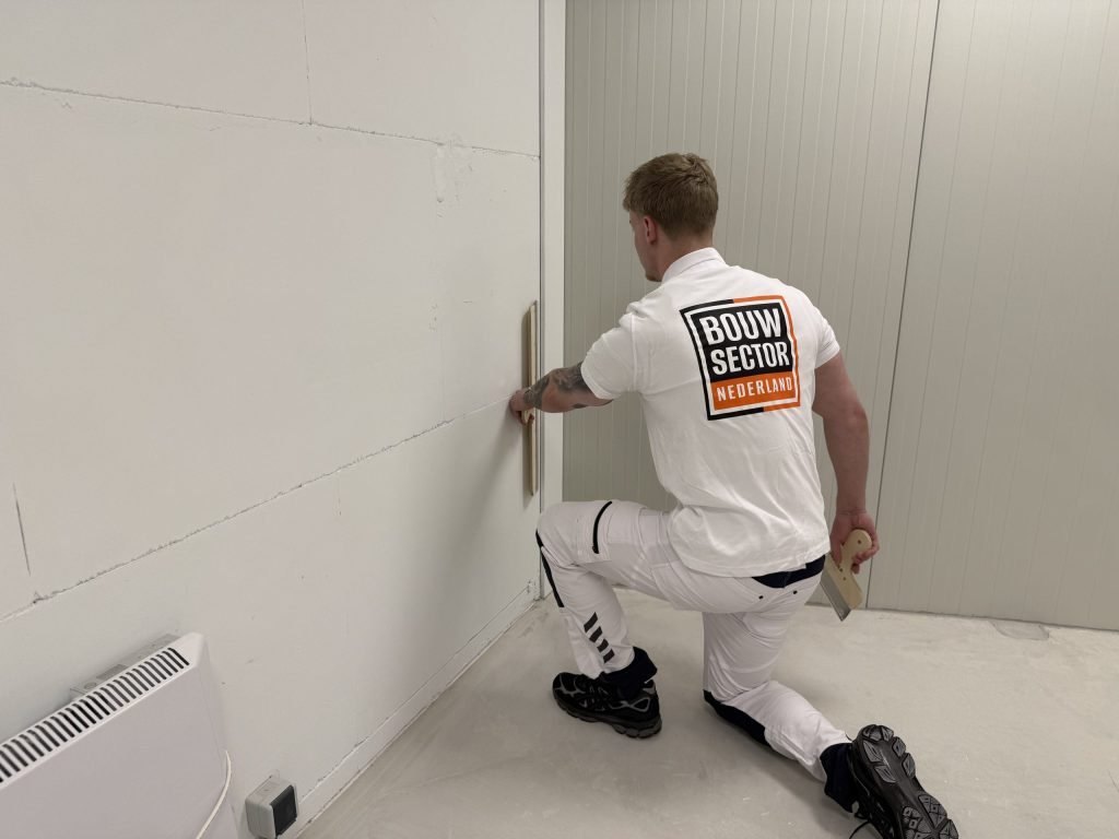Stukadoor van Bouwsector Nederland zit op een knie en trekt met de spaan het onderste deel van een muur recht