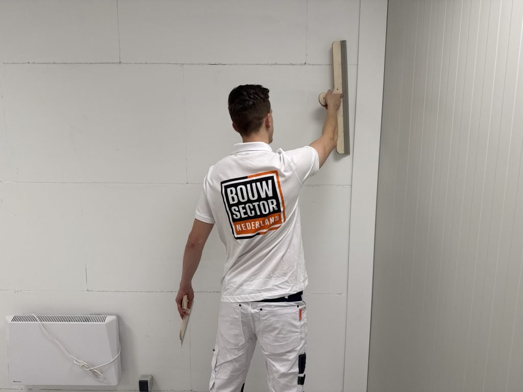 Stukadoor van Bouwsector Nederland met een lange spaan tegen een gipsplaatwand waarop de naden nog te zien zijn